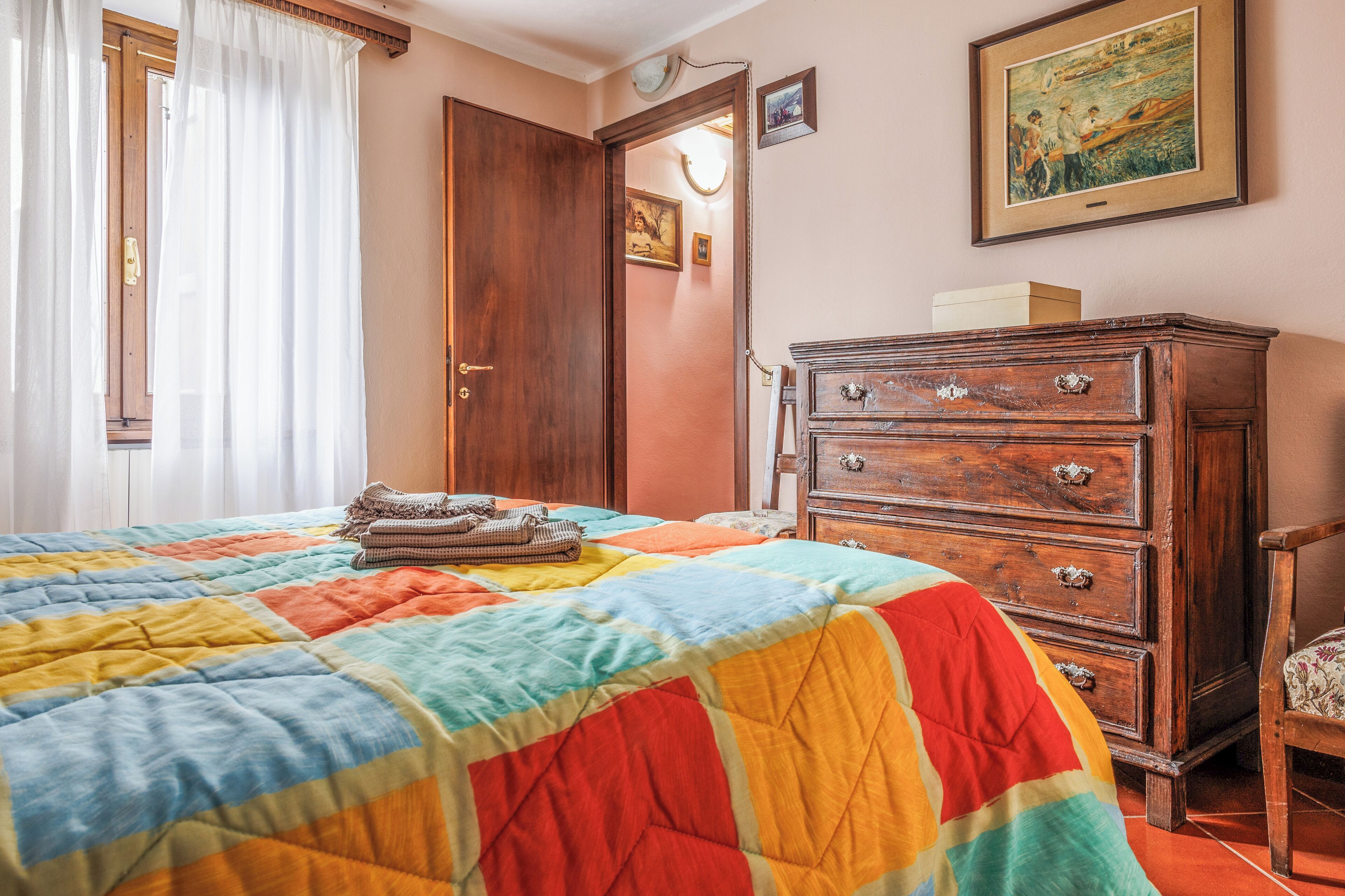 Een slaapkamer met een kleurrijk geborgd bed, een houten dressoir en een deur naar een andere kamer.
