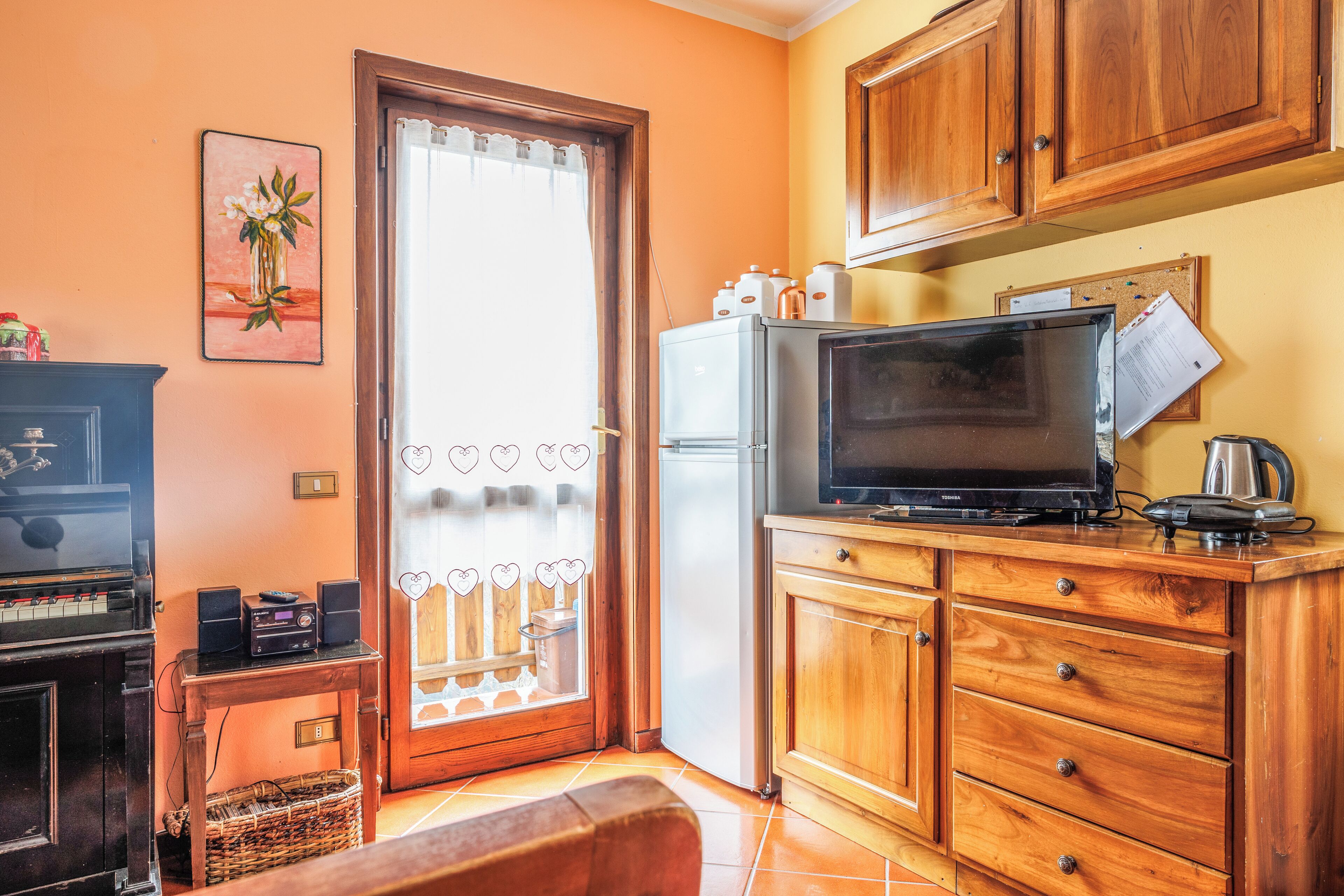 A compact kitchen with wooden cabinets, a refrigerator, a microwave, and a piano.