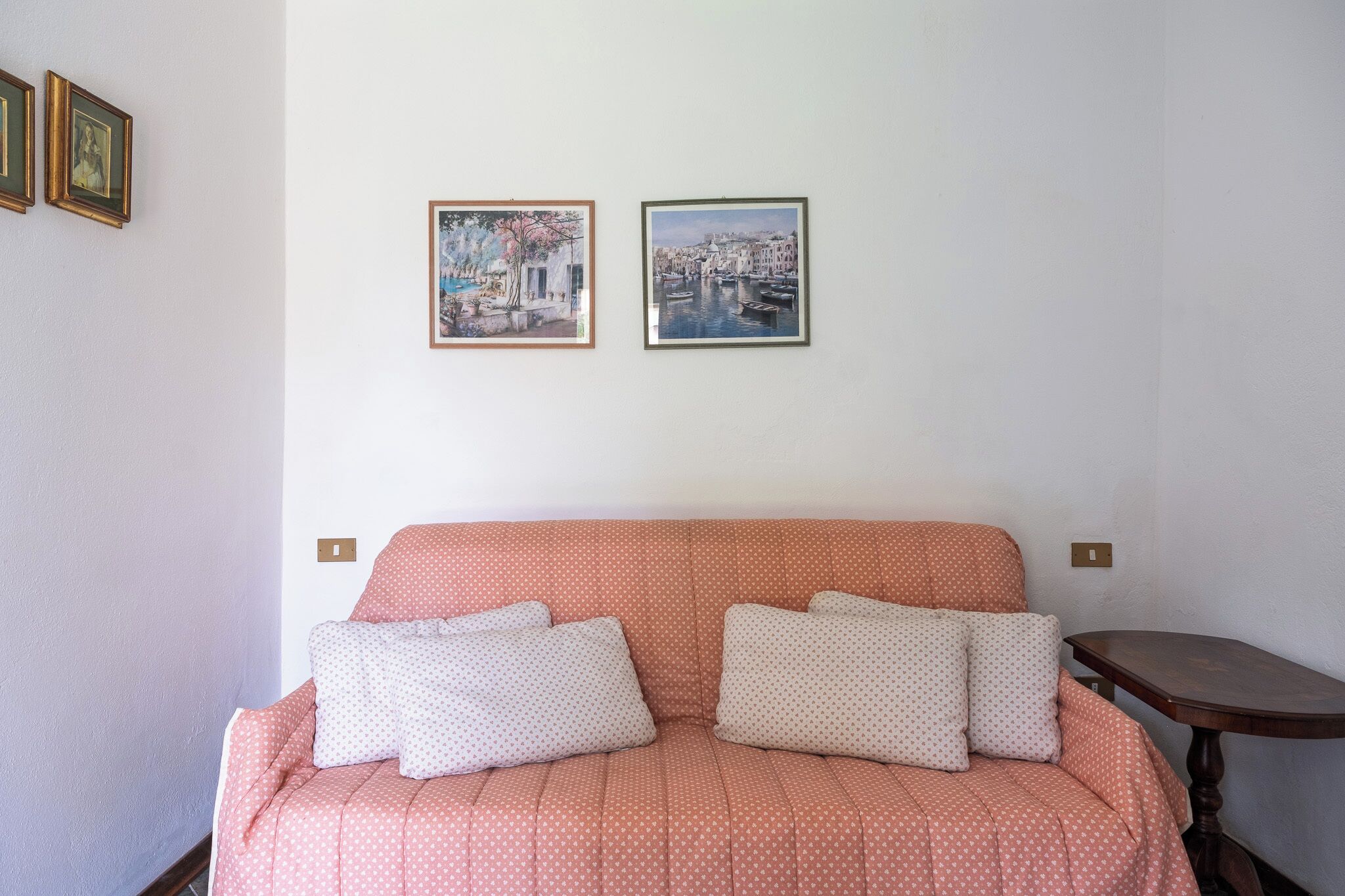 A room with a pink polka-dotted sofa, two framed artworks on the wall, and a small wooden table.