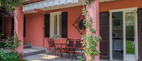 A pink building with a covered patio, black shutters, and a table with chairs.