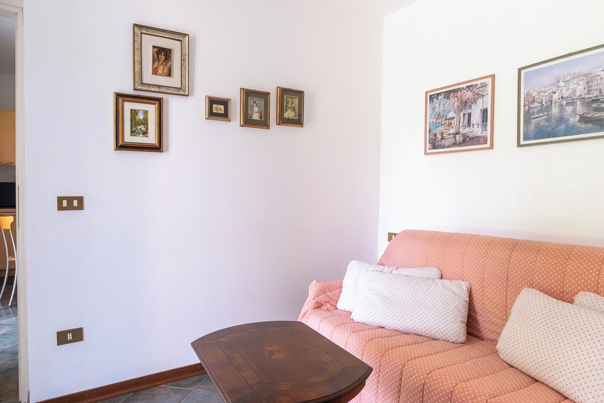 Un salon avec un canapé rose, une table basse en bois et quatre tableaux encadrés accrochés au mur.