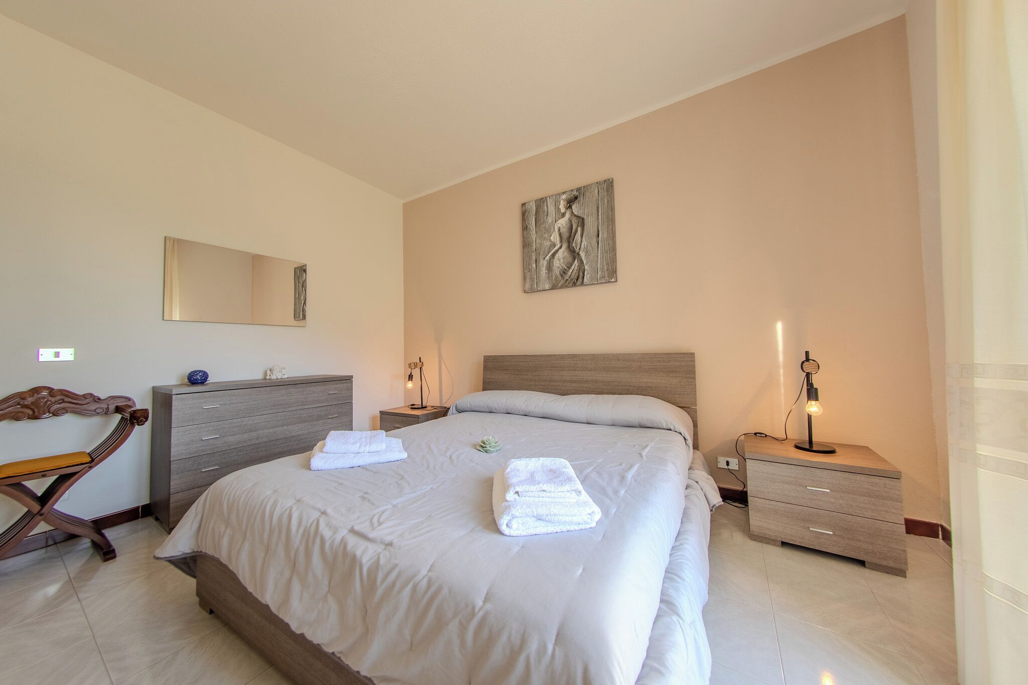 Un dormitorio ordenado con una cama, una mesita de noche con lámpara, un aparador y un espejo montado en la pared.