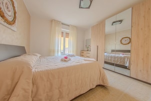 Un dormitorio con cama, armario, espejo y ventana con cortinas.
