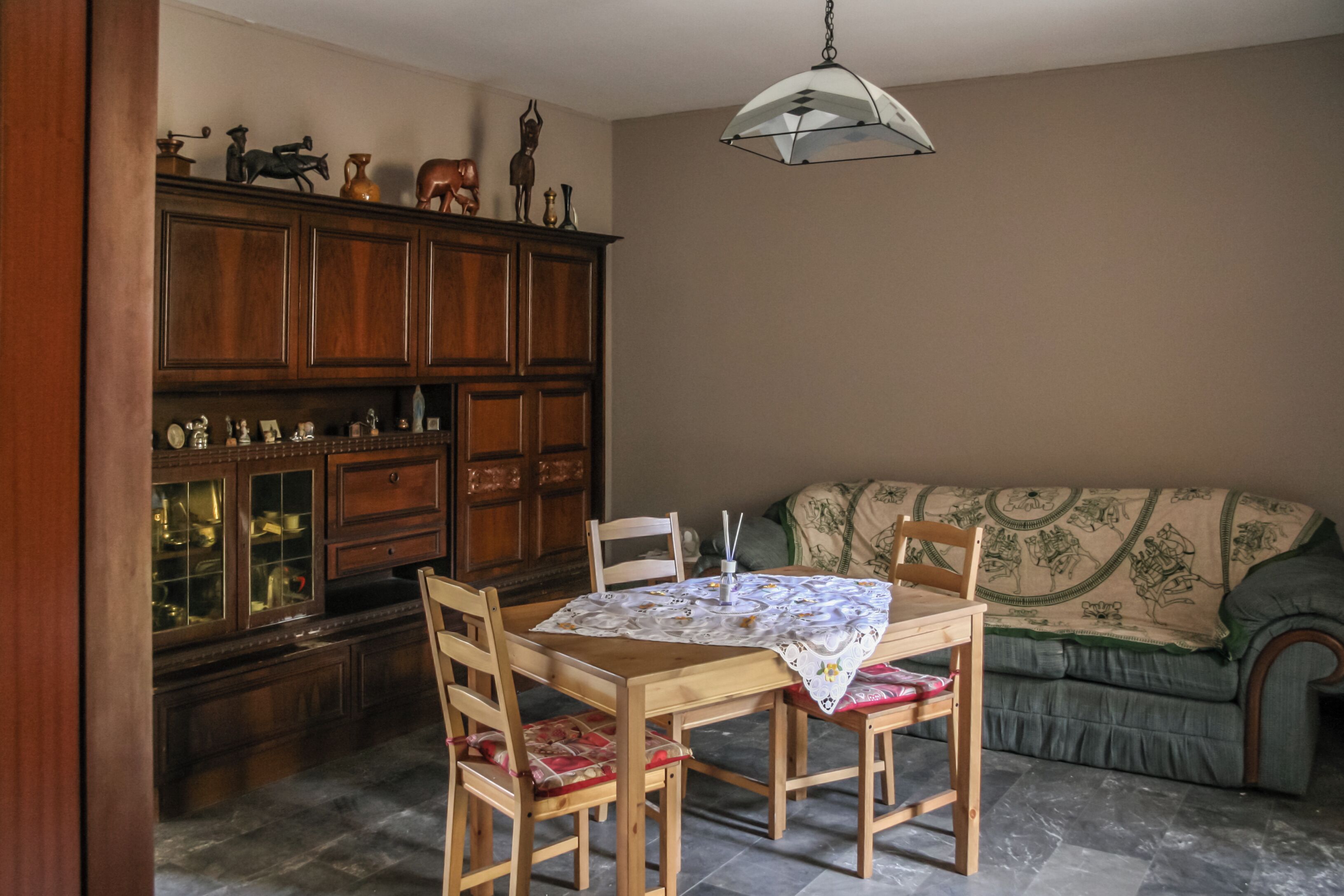A dining area with a wooden table and chairs, a cabinet with glass doors, and a patterned sofa.