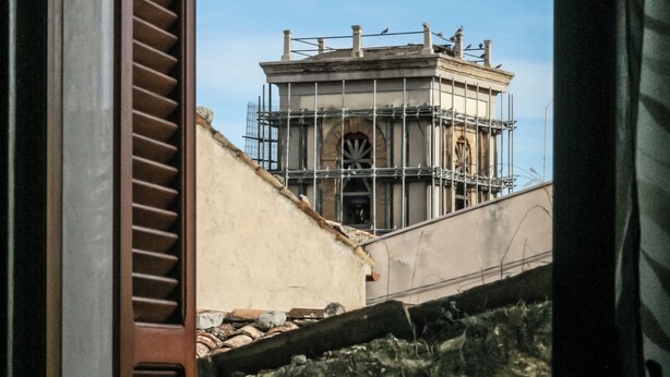 A view through a window with a wooden shutter, revealing a stone wall and a building under construction with scaffolding. - Brother'S Home (Civitella Casanova)