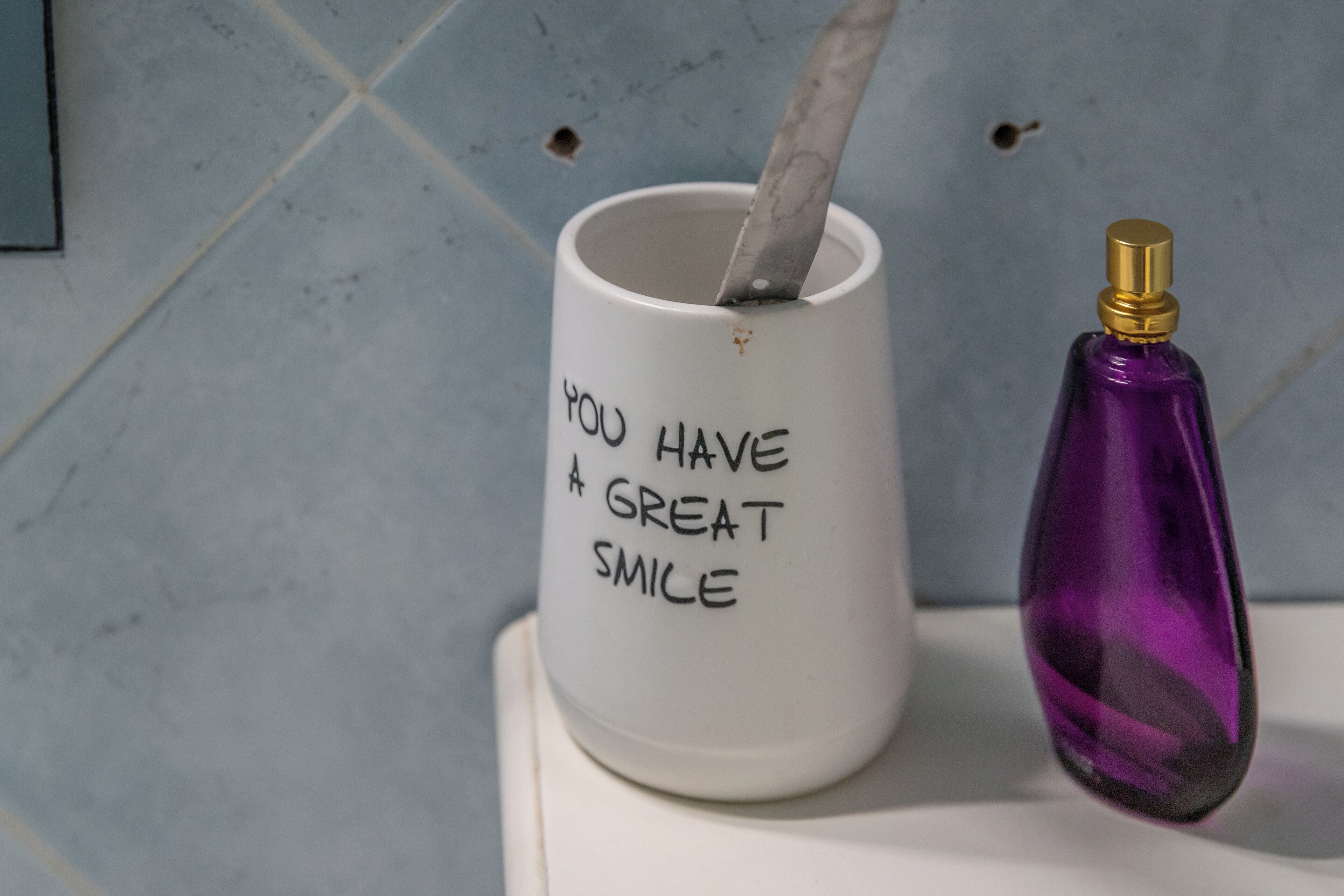 A white mug with a spoon and a purple bottle with a gold cap on a white surface.