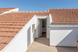 Una habitación bajo los tejados, estrecha, con techo de tejas y una puerta que da a un pasillo.
