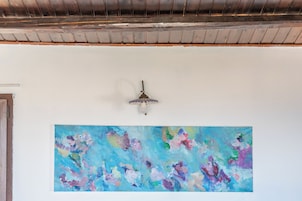 Una habitación con un cuadro abstracto grande en la pared, un ventilador de techo y una puerta de madera.