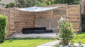 Een terras met houten omheining, een zithoek en een tuin met bloemen en struiken.