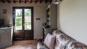 Een gezellige woonkamer met een houten plafond, een bloemenbank, een televisie en een deur naar een tuin.