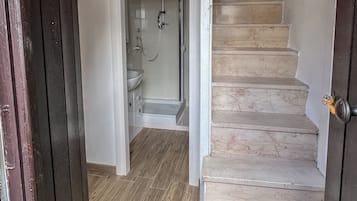 A staircase leading to a bathroom with a shower and a sink.