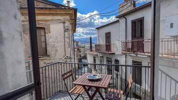 A balcony with a table and chairs, overlooking a street with buildings and a clear sky.