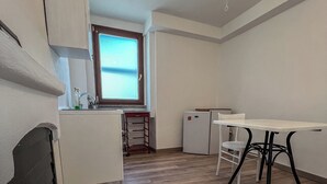 Una cocina compacta con ventana, una mesa de comedor con sillas y un refrigerador pequeño.