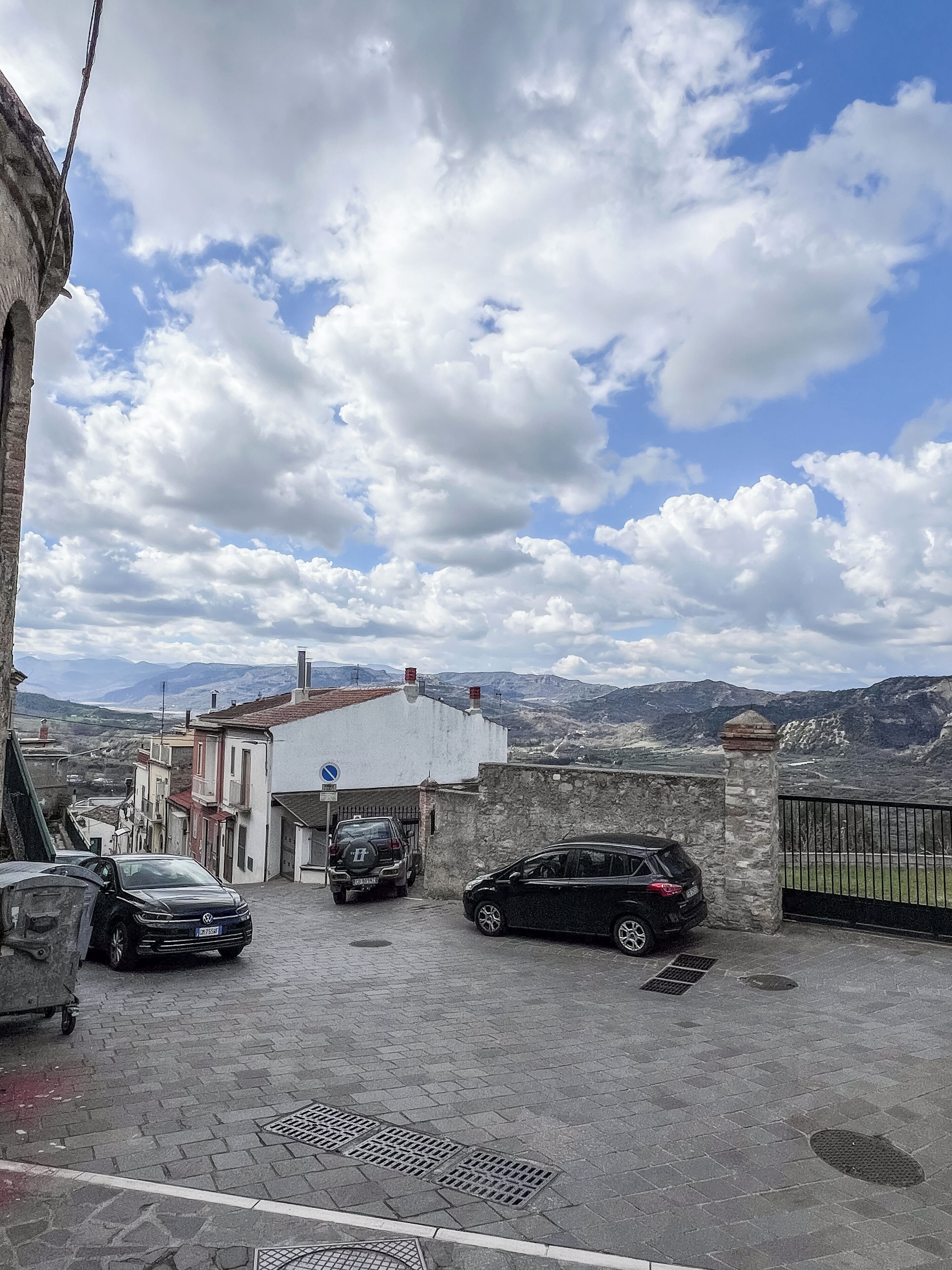 Un'area di parcheggio con due auto, un edificio bianco e un muro in pietra.