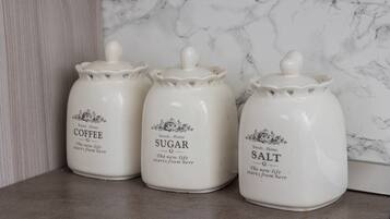 Tres recipientes de cerámica blanca con tapas, etiquetados 'Coffee', 'Sugar' y 'Salt', sobre una encimera de cocina con salpicadero de mármol.