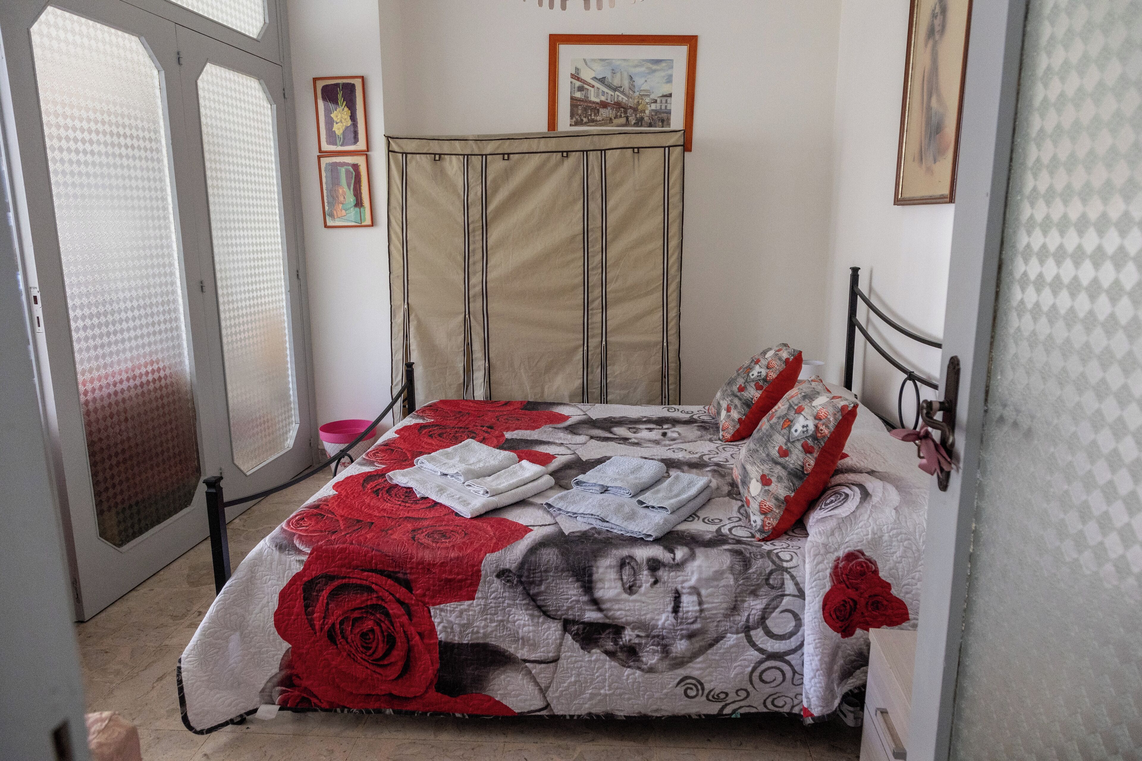 Un dormitorio con cama, una ventana con persianas, una puerta y una pared decorada con marcos.