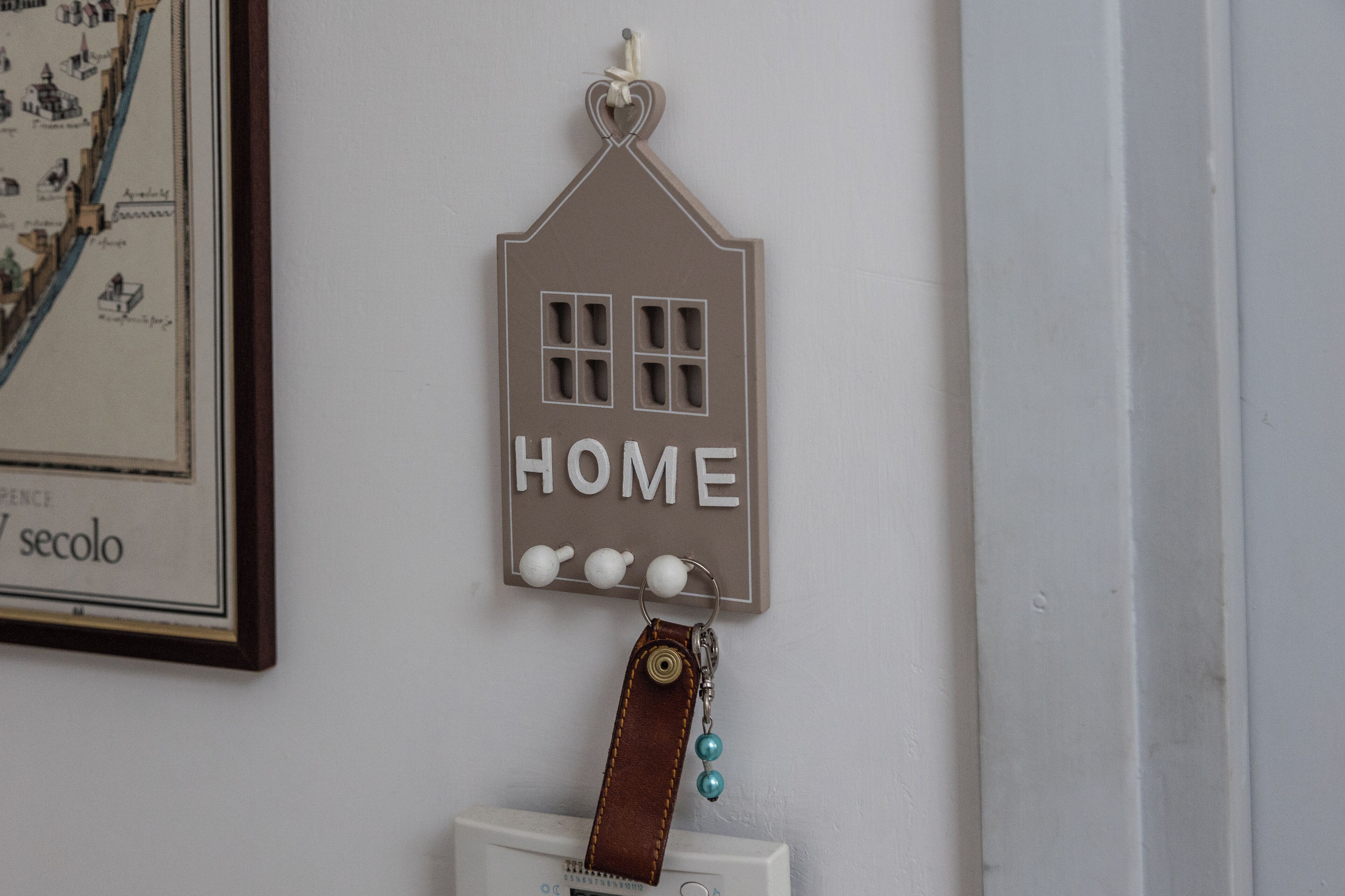 Un élément de décoration à fixer au mur, en forme de maison, sur lequel est inscrit le mot « HOME ».
