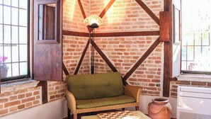 A cozy room with exposed brick walls, a wooden ceiling, and a green cushioned chair. - Antica Cantina Emilia (Reggio Calabria)