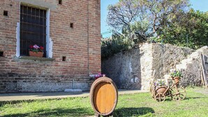 A brick building with a window, a wooden barrel, and a cart with pots. - Antica Cantina Emilia (Reggio Calabria)