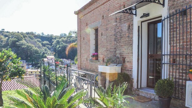 A brick building with a balcony, potted plants, and a view of a hillside. - Antica Cantina Emilia (Reggio Calabria)