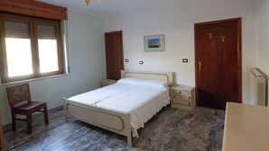 A bedroom with a bed, a chair, a wooden wardrobe, a nightstand, a radiator, and a window with blinds. - La Vecchia Cascina (Atena Lucana)
