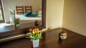 Une commode en bois avec un miroir qui reflète un lit avec un oreiller bleu et une fenêtre donnant sur une balustrade.