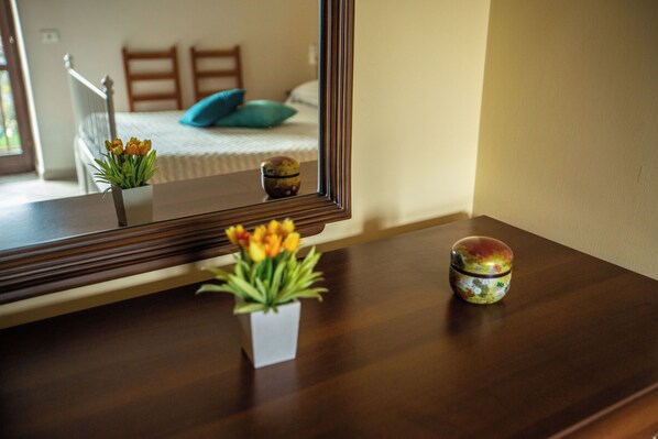 Een houten dressoir met een spiegel, waarop een bed met een blauw kussen en een raam met uitzicht op een leuning te zien is.