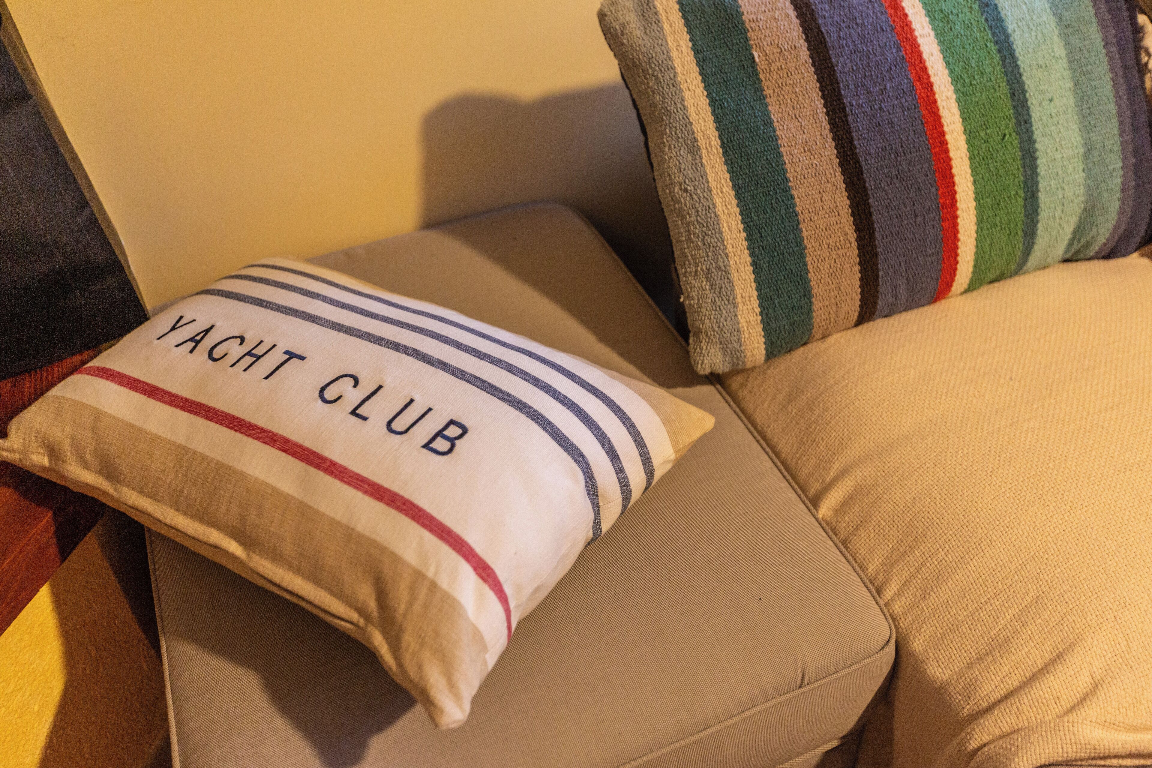 Un canapé beige agrémenté d’un coussin sur lequel est inscrit « YACHT CLUB » et d’un autre coussin à rayures.