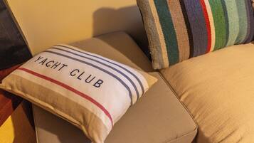 Un canapé beige agrémenté d’un coussin sur lequel est inscrit « YACHT CLUB » et d’un autre coussin à rayures.
