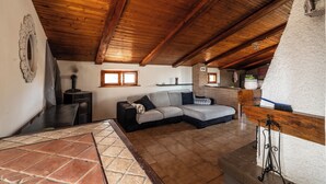 Acogedor dormitorio en el ático con techo de madera, un sofá, chimenea y pared de piedra rústica.
