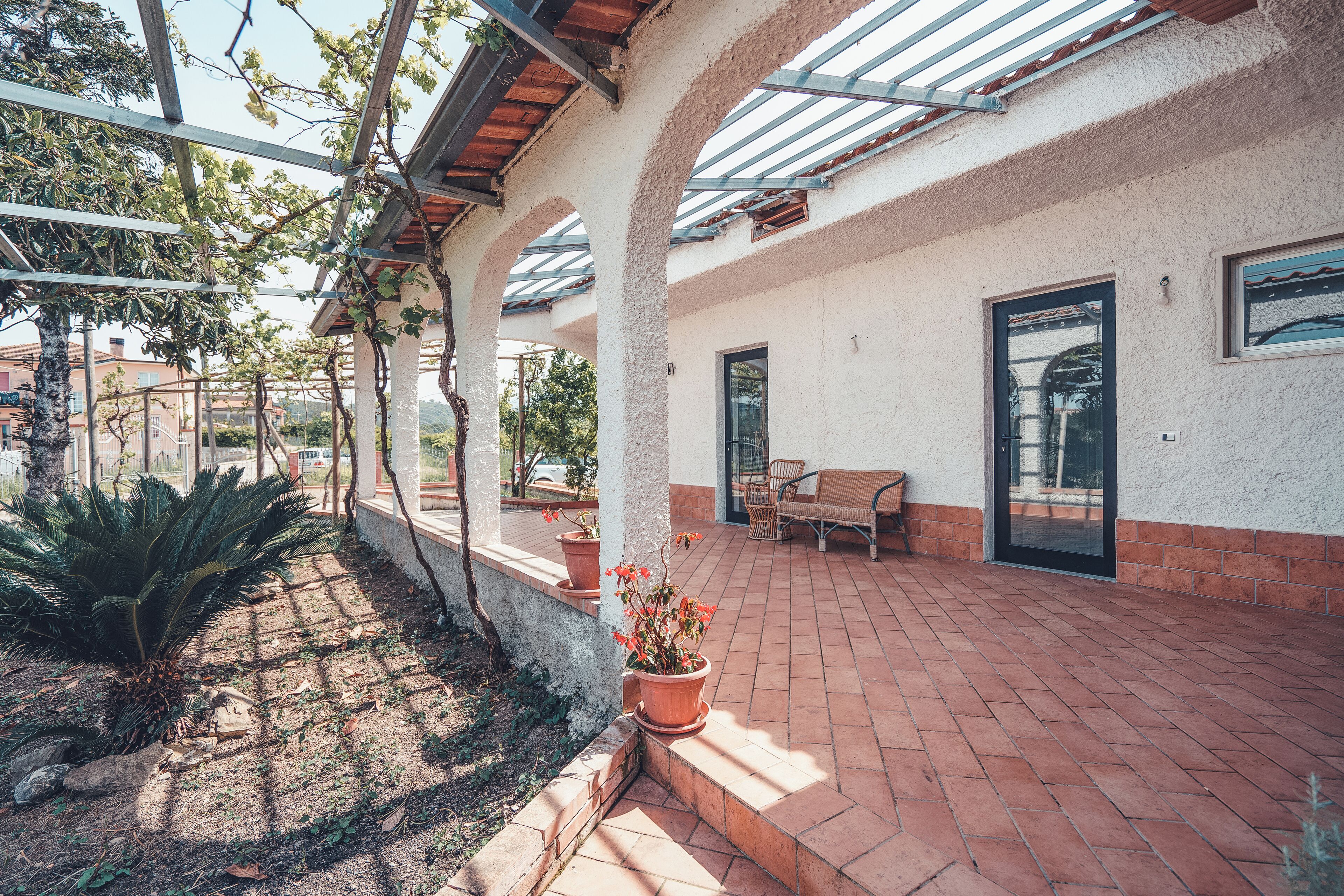 A covered patio area with brick flooring, potted plants, and a bench.