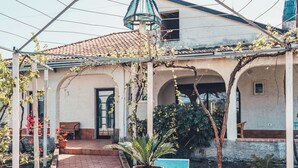A covered patio area with a tiled floor, two blue chairs, a table, and a hanging light fixture.