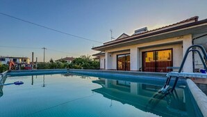 A swimming pool with a clear blue surface, a ladder, and a house with a tiled roof in the background.