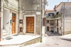 Une rue étroite avec une porte en bois, une enseigne indiquant « VIA POGGIO », et un immeuble doté d’un balcon.