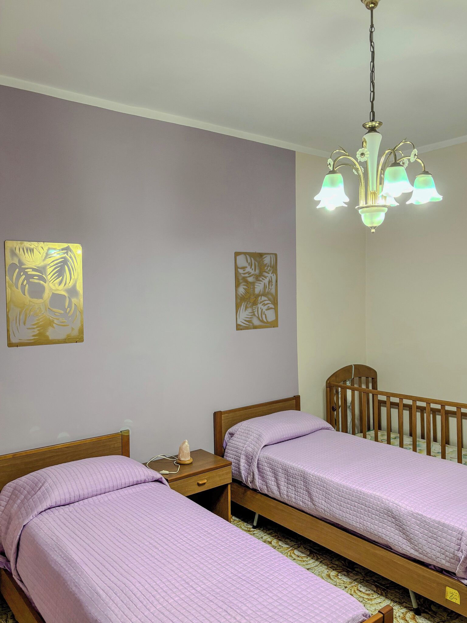 Een slaapkamer met twee enkele bedden, een houten ledikant, een nachtkastje en een kroonluchter.