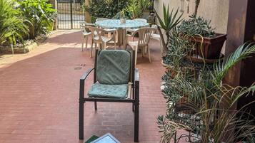 A patio area with a table and chairs, surrounded by potted plants and a brick floor.