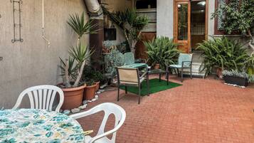 Eine Terrasse mit Pflasterboden, Blumentöpfen, einem Tisch mit floralem Tischläufer und zwei Stühlen.