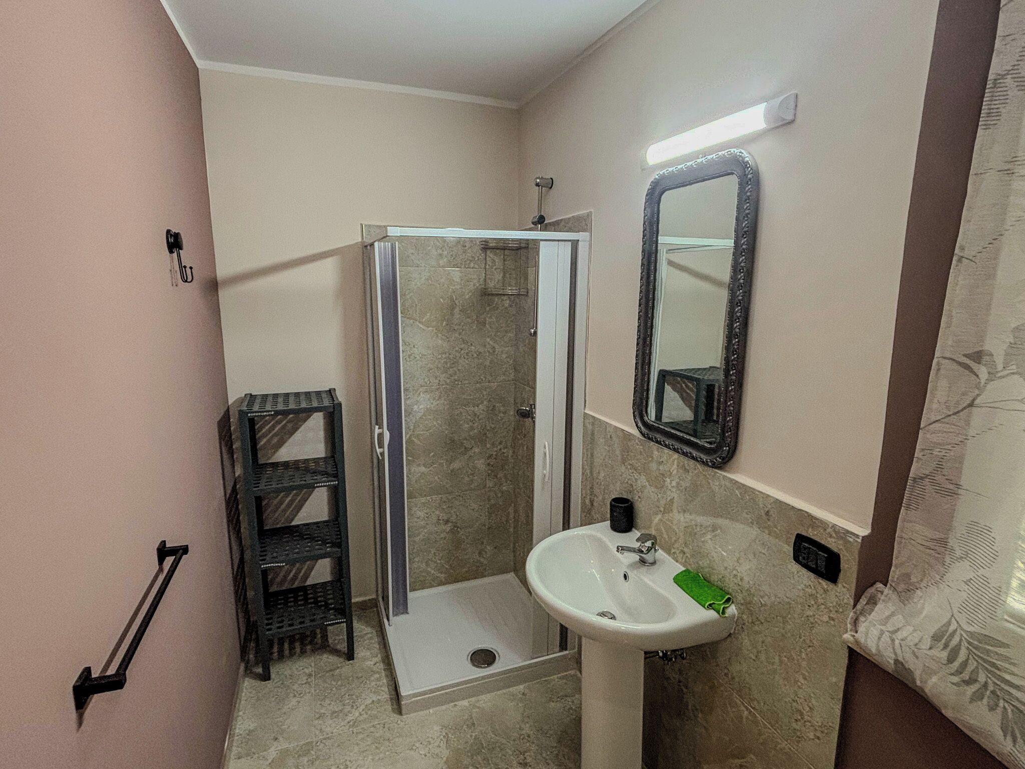 A bathroom with a glass shower enclosure, a sink with a green towel, and a mirror with a decorative frame.