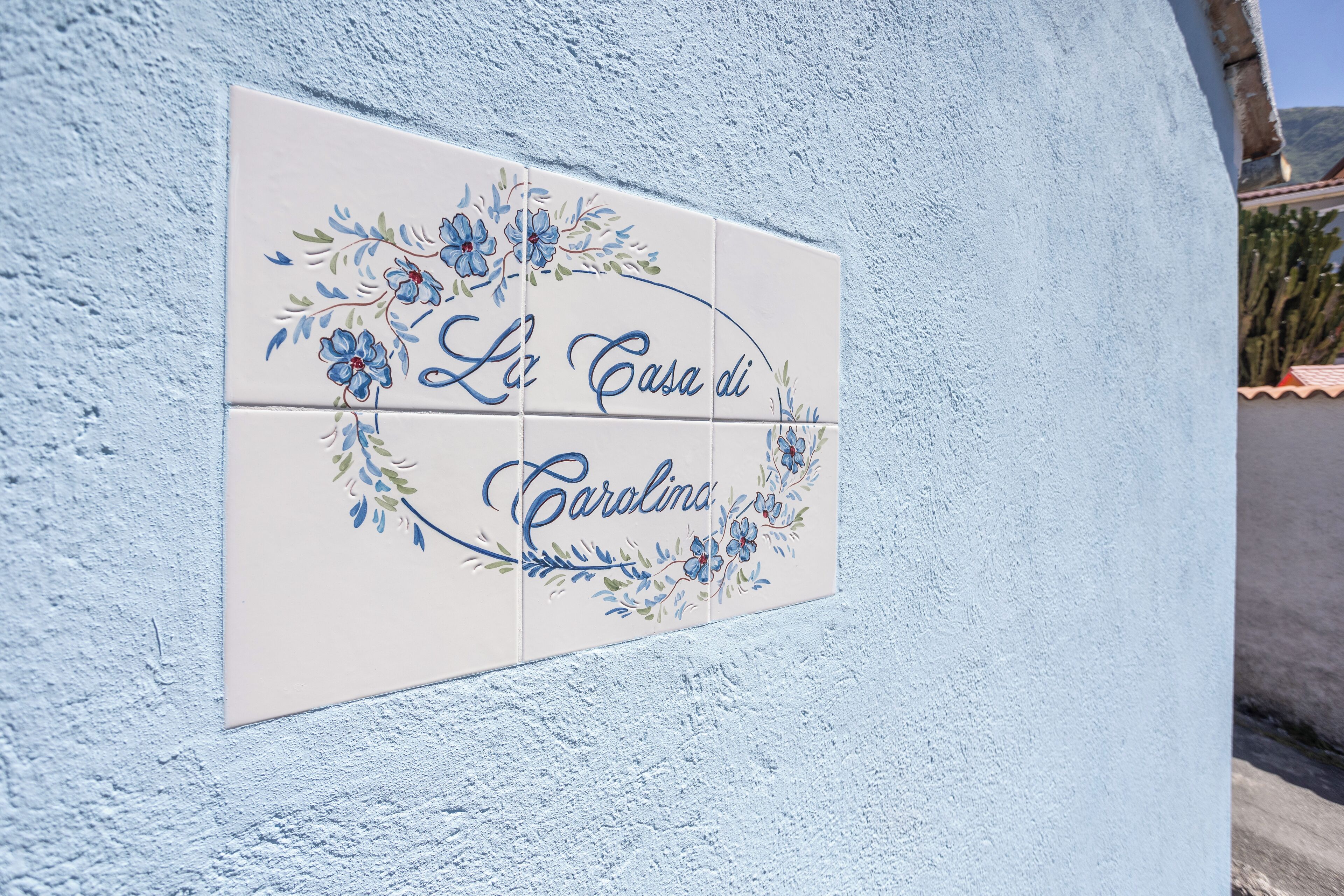 A tiled sign with floral designs and the text "La Casa di Carolina" on a light blue wall.