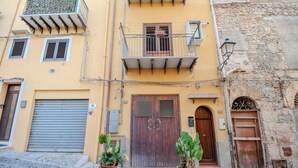 A two-story building with a wooden door, a balcony with metal railings, and potted plants in the foreground. - La Discesa Di San Giuseppe (Termini Imerese)