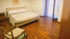 A bedroom with a large bed, a wooden chair, a radiator, and a balcony. - La Discesa Di San Giuseppe (Termini Imerese)