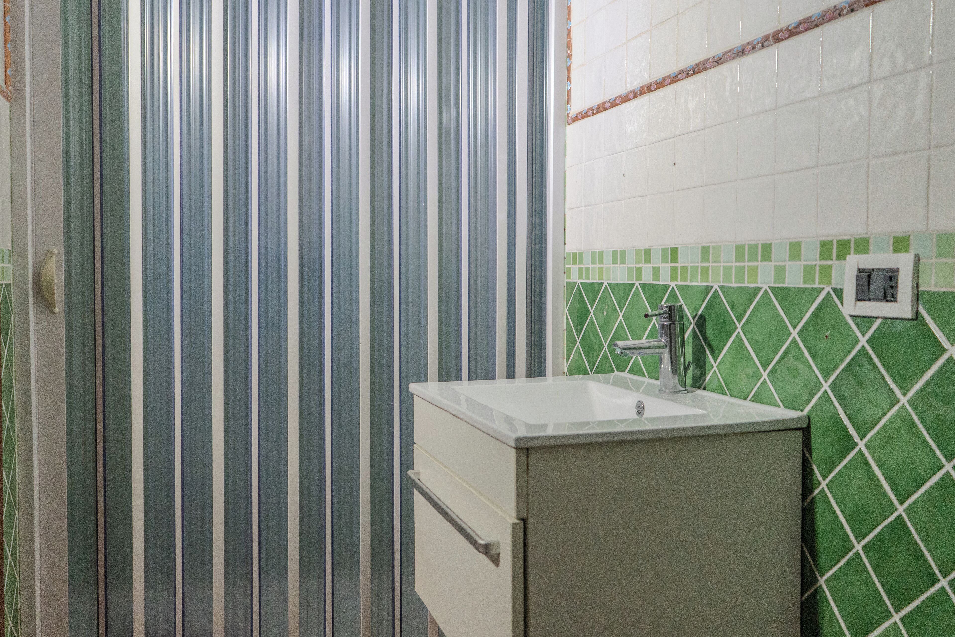 A bathroom with a striped shower curtain, a sink with a faucet, and green and white tiled walls.