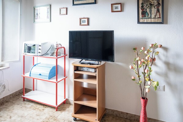 A room with a TV on a stand, a red and blue cart, and a vase with flowers. - Casa Nonna Ica (Tresnuraghes)