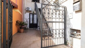 Una entrada con reja metálica, una planta en maceta y una escalera que lleva a una puerta.
