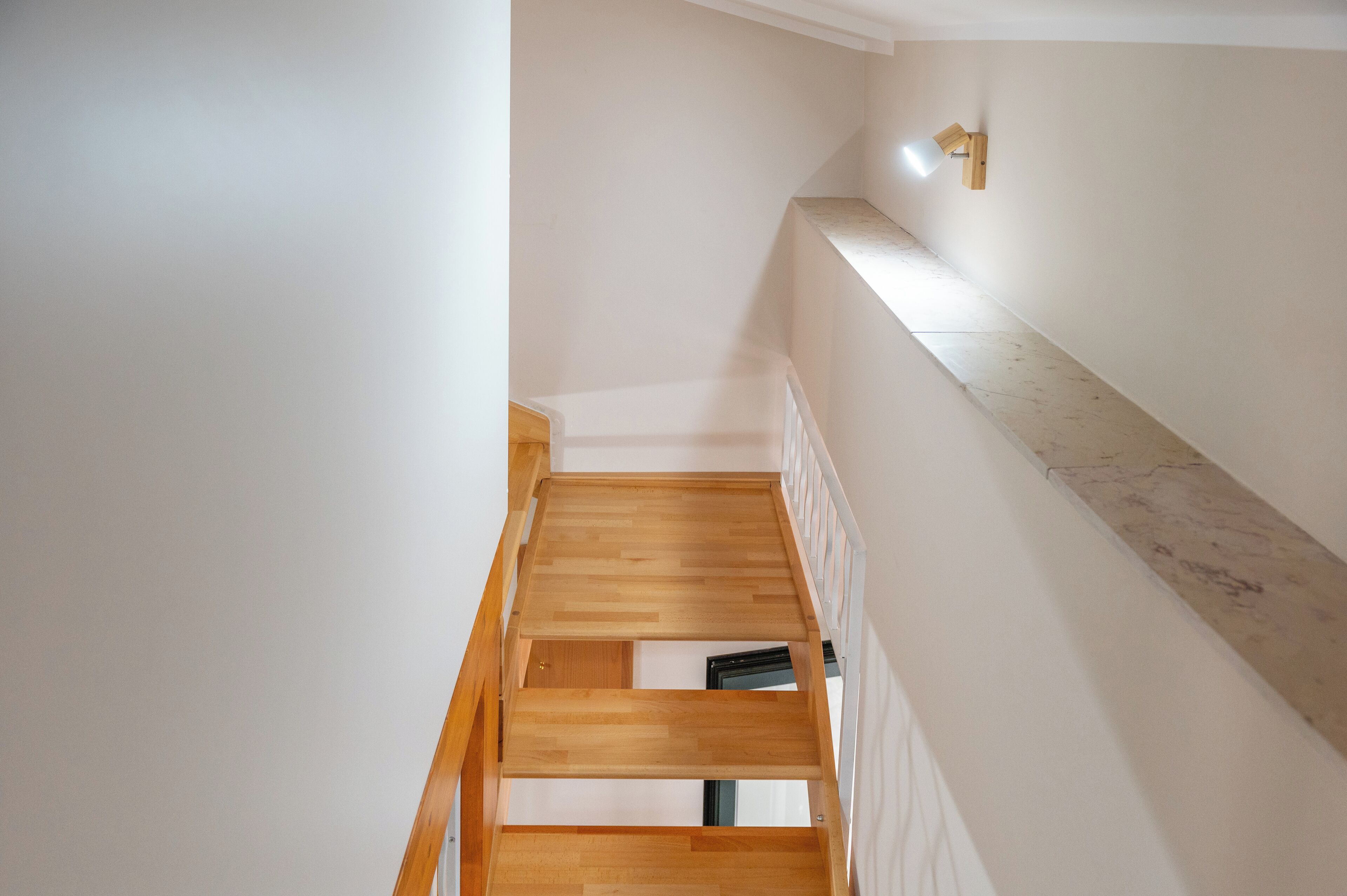 Una escalera estrecha con escalones de madera y paredes blancas.