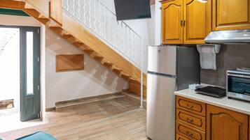 Una cocina con armarios de madera, un refrigerador, un microondas y una escalera con barandilla de madera.