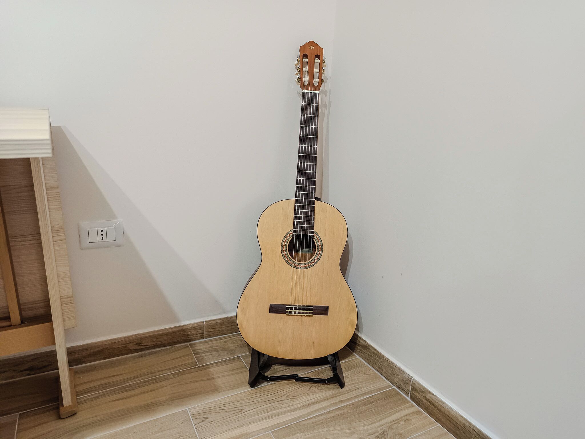 Una guitarra acústica sobre un suport negre davant d'una paret blanca.