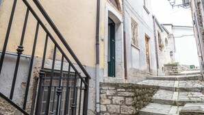 A narrow street with stone steps leading to a building with a green door and a window with a metal grille. - Sant'Janni (Buonalbergo)