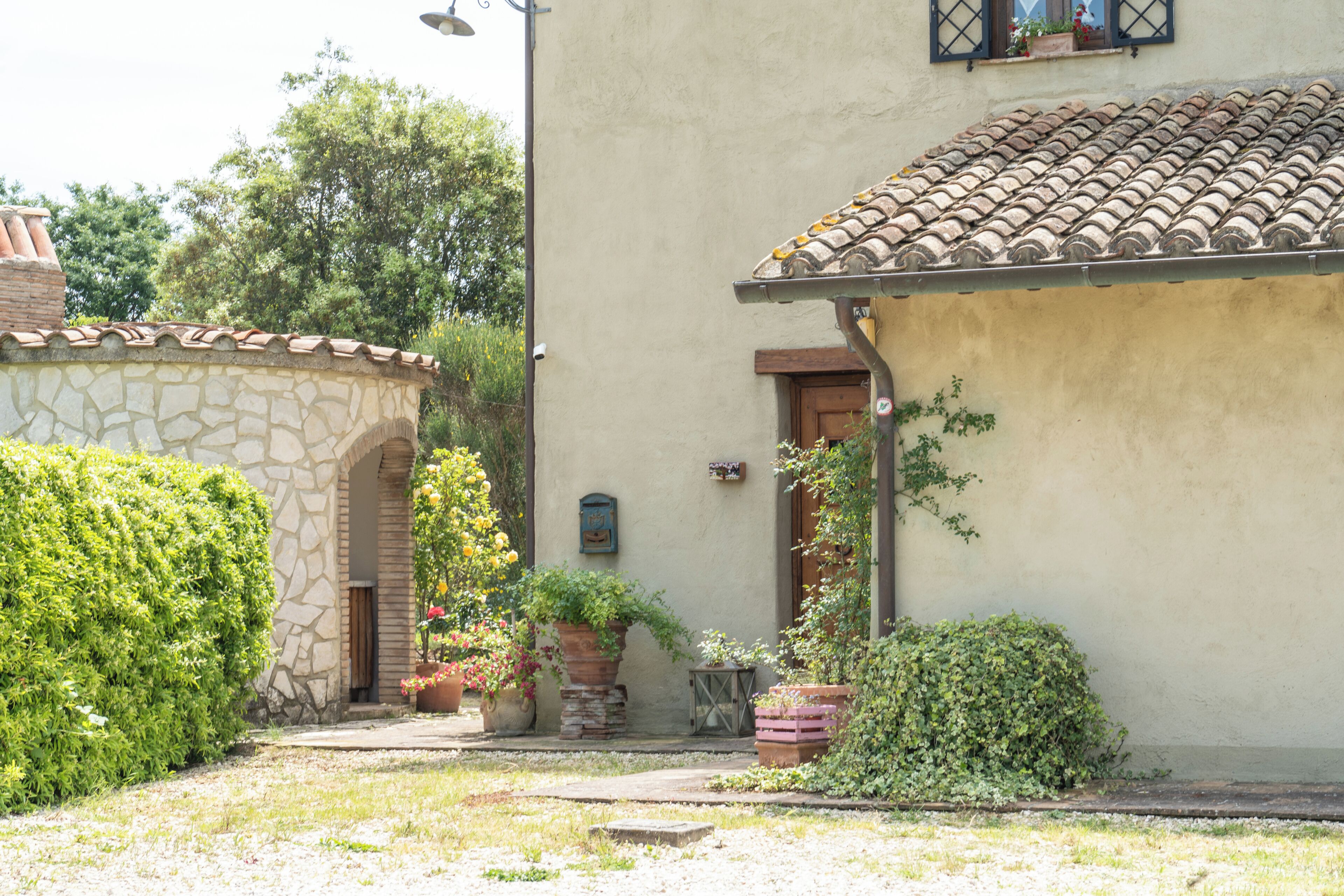 A courtyard with a stone archway, a tiled roof, and potted plants.