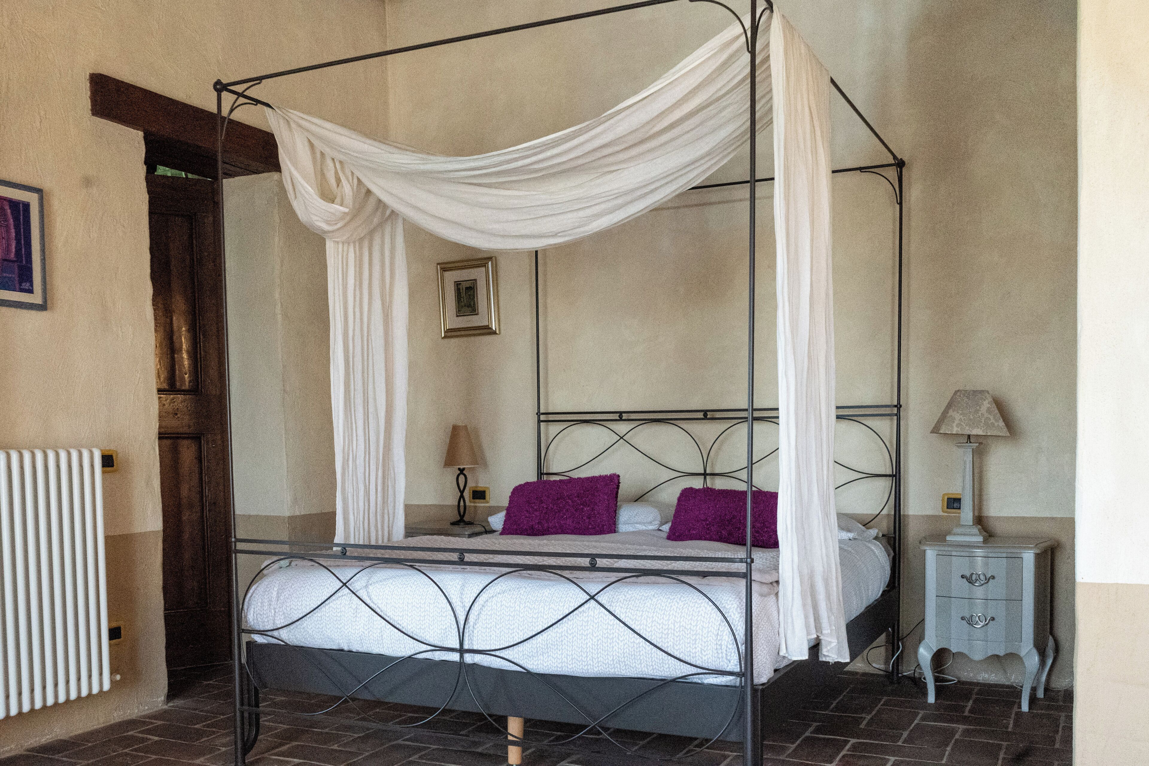 A four-poster bed with a canopy, a bedside table with a lamp, and a picture on the wall.